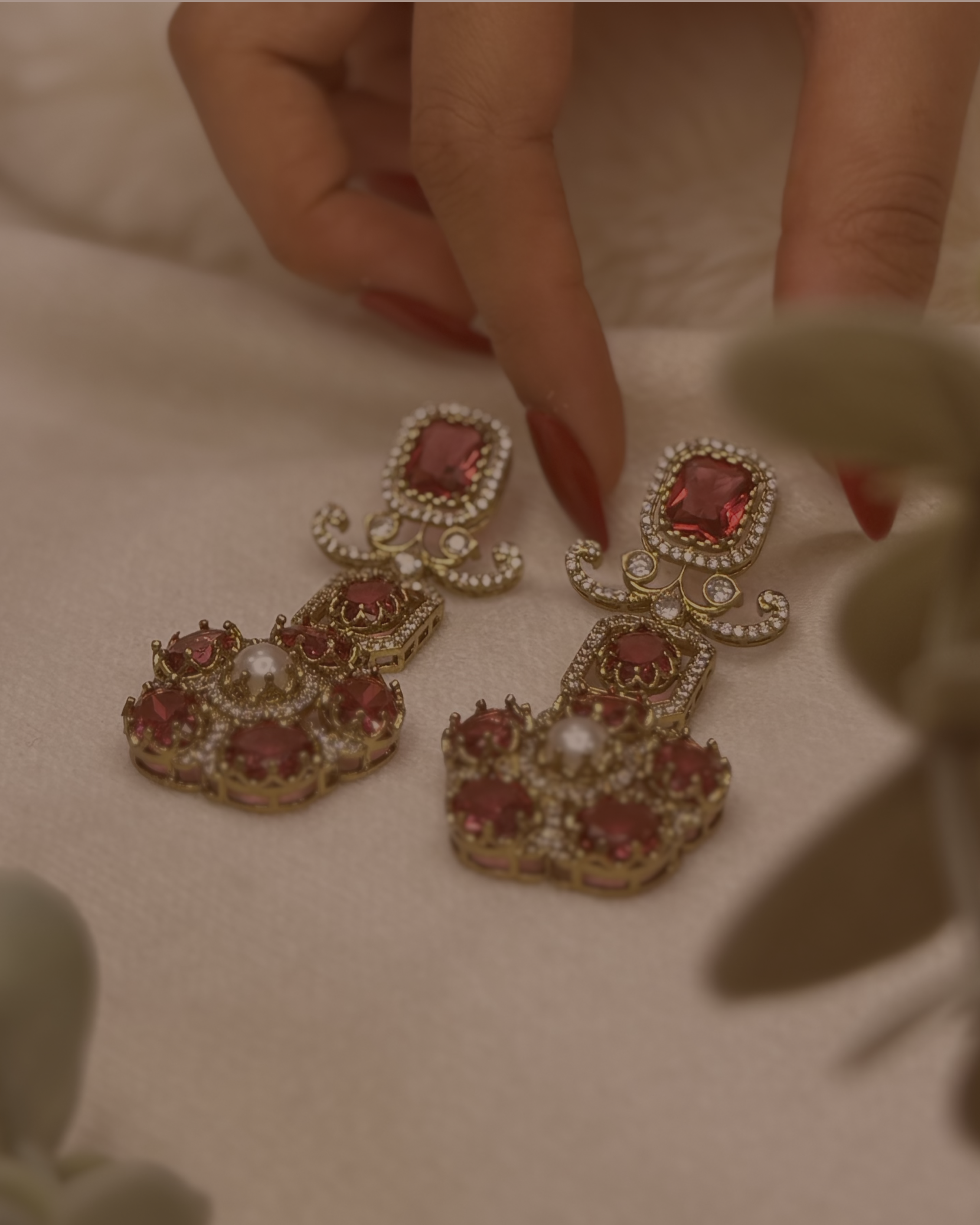 Ornate earrings with red gemstones and gold accents on a neutral background