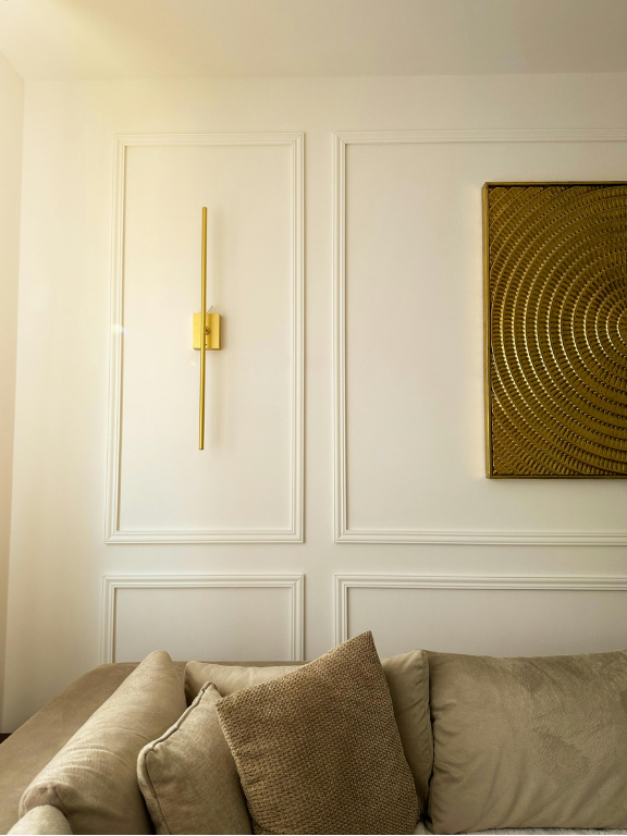 Decorative wall sconce and abstract painting on a white paneled wall with a beige sofa.